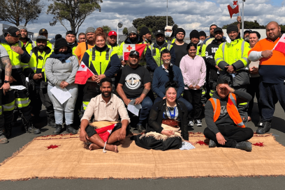 Group photo of Lineage Auckland team members in New Zealand, gathered outdoors, showcasing diversity with various team members holding flags and wearing safety vests, reflective of a multicultural workplace.